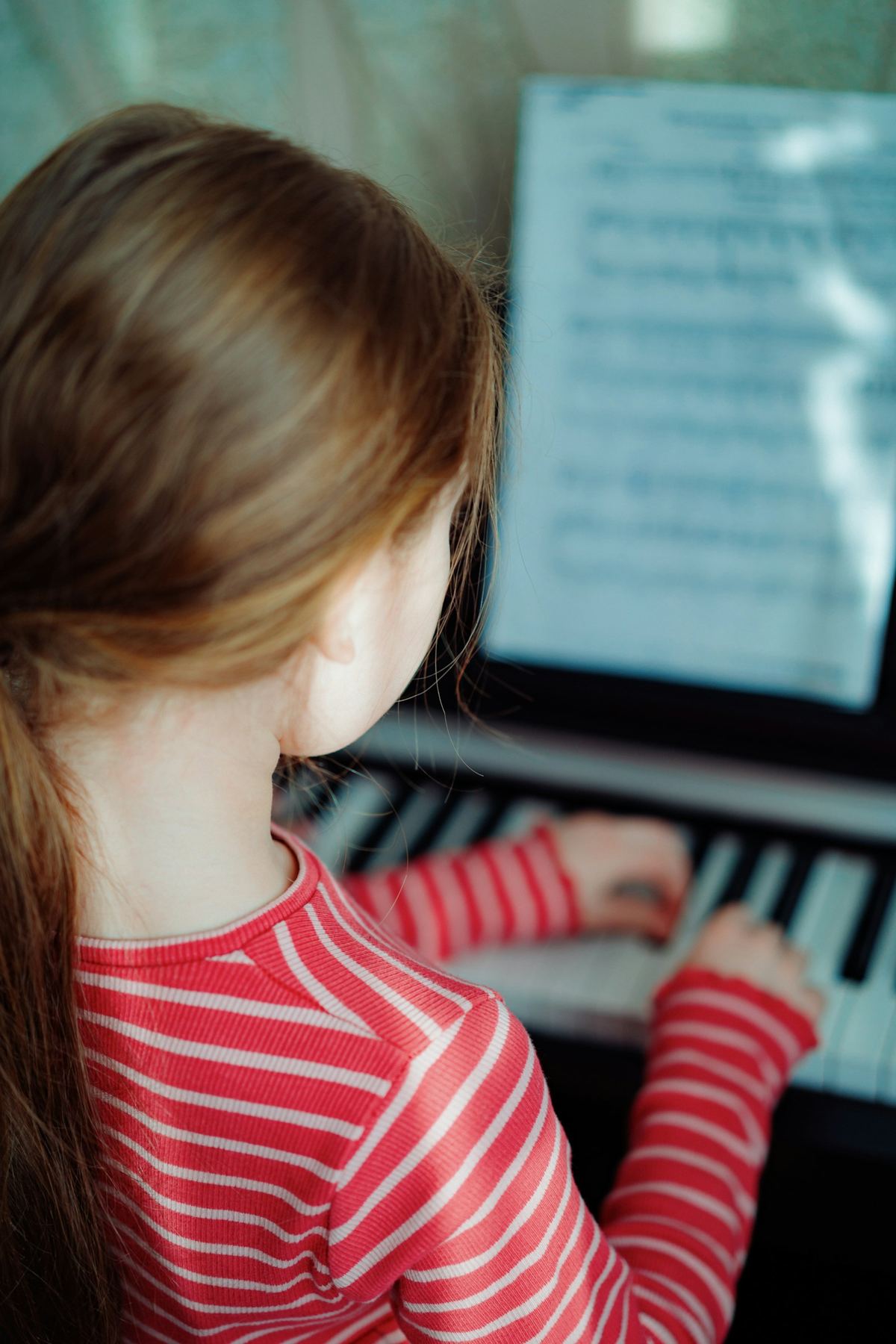 A young girl reads sheet music while playing the piano