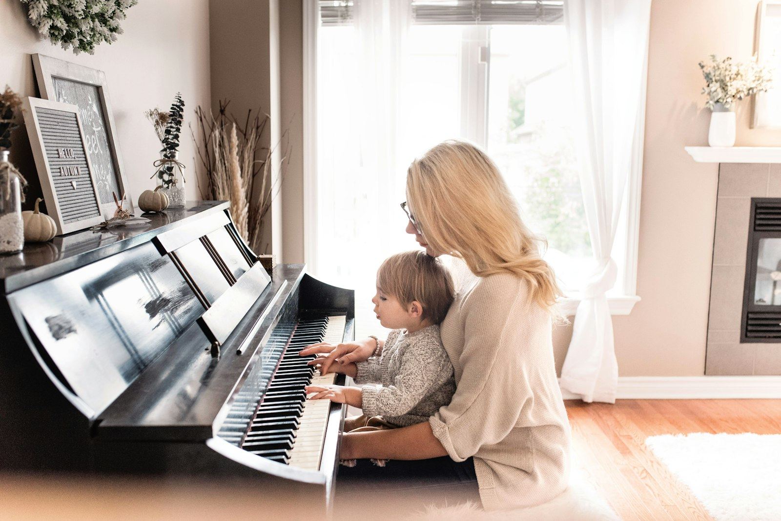 A teacher and a young child playing piano together in a bright room